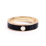 A Marcello Riccio ring with a black enamel band, rose gold metal borders, and a single round clear gemstone on the front, shown on a BLACK background.